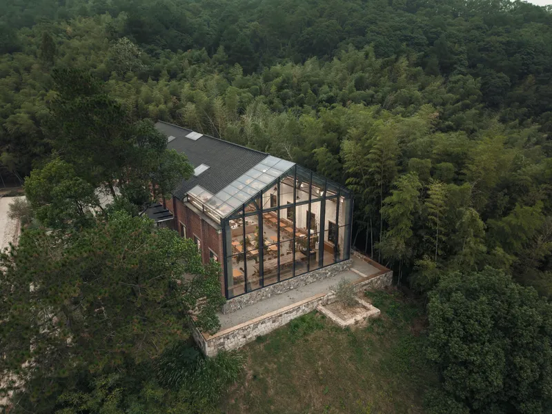 Aerial view of the gabled glass and steel pavilion nestled in a hillside forest