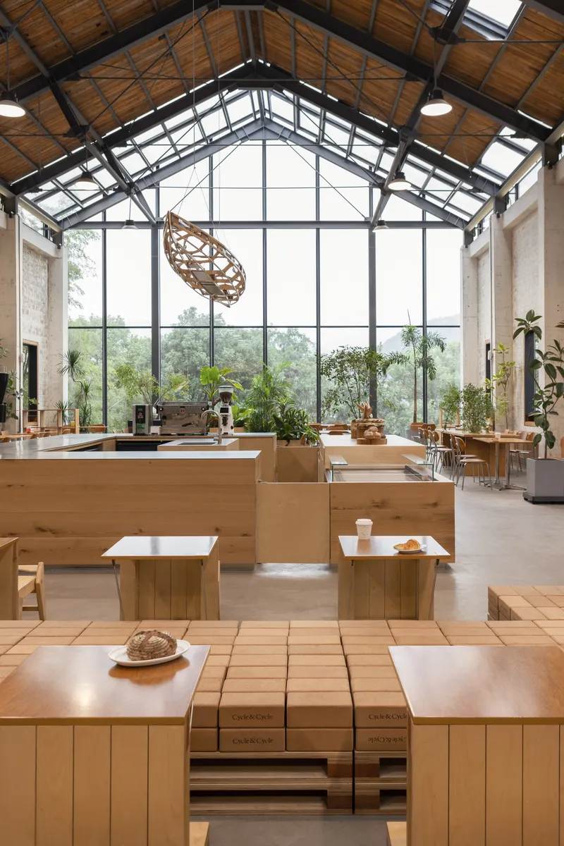 View toward the glazed gable end with suspended timber sculpture and potted plants on terracotta tile floor