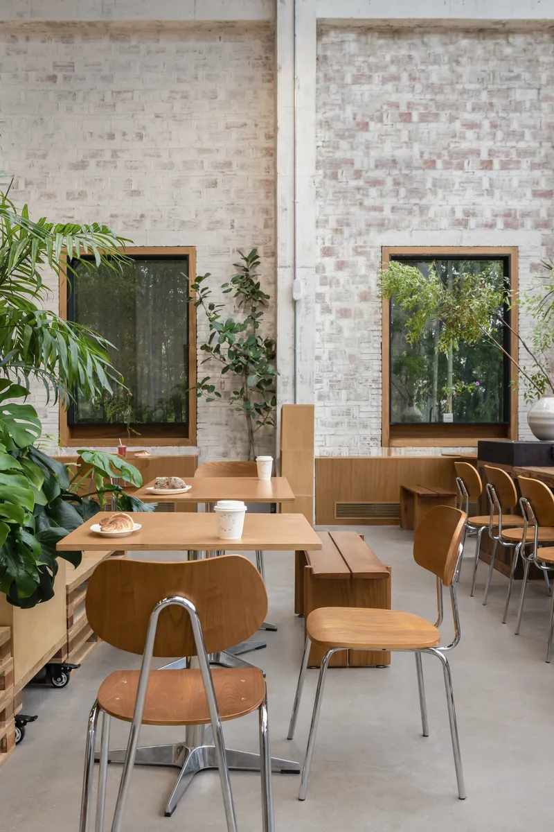 Dining area with pale brick walls, timber-framed windows and movable wooden tables among indoor plants