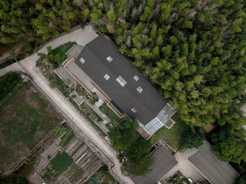 Aerial view of the dark corrugated metal roof with skylights surrounded by dense forest