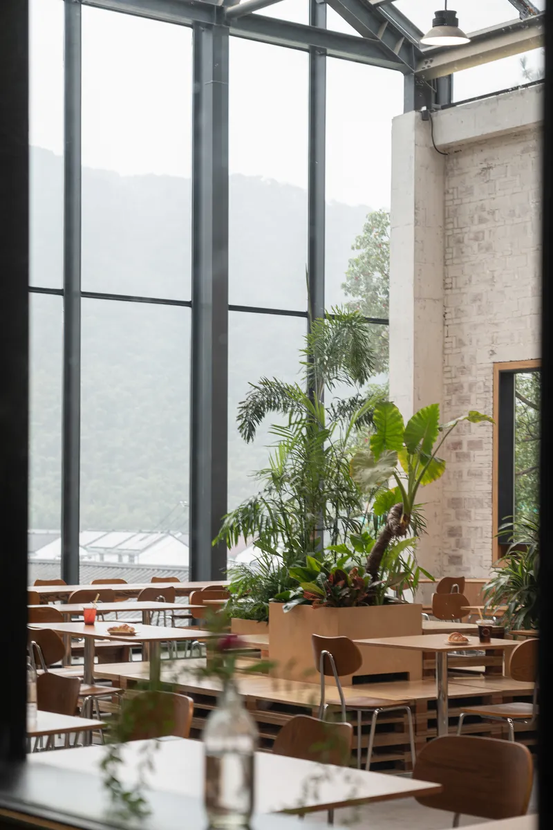 Seating area with floor-to-ceiling steel-framed windows and planted beds looking toward distant mountain range
