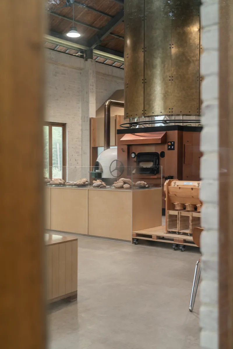 View through doorway to bakery counter with copper oven enclosure and brass chimney flue above