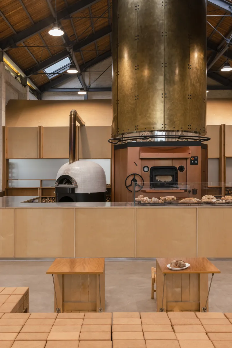 Bakery workspace with white-tiled dome oven, copper deck oven and brass flue under timber ceiling
