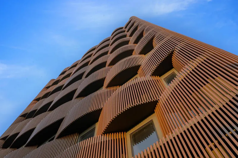 Close-up of the ribbed terracotta cladding wrapping around the curved corner balconies at dusk