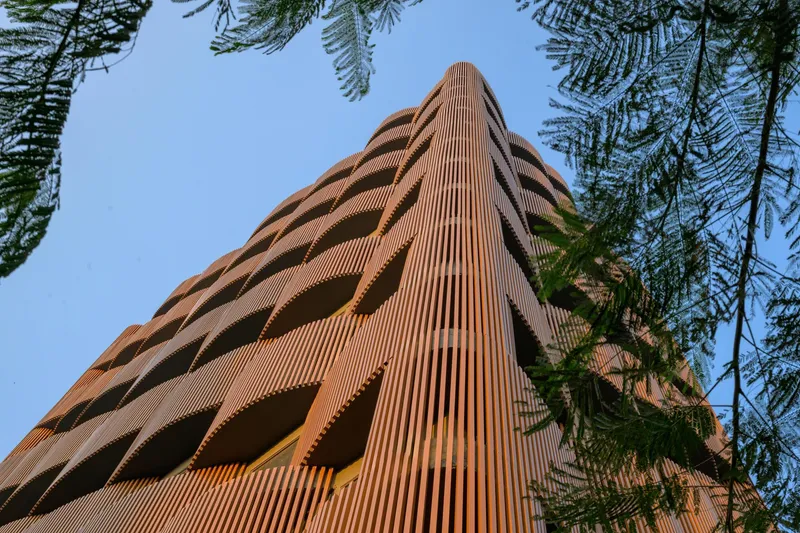 Corner view of the terracotta-clad tower rising through overhanging tree branches in afternoon light