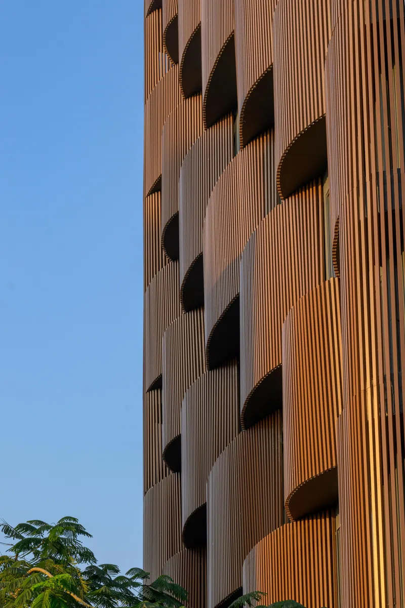 Detail of vertical terracotta fins wrapping the facade edge with tree foliage in foreground