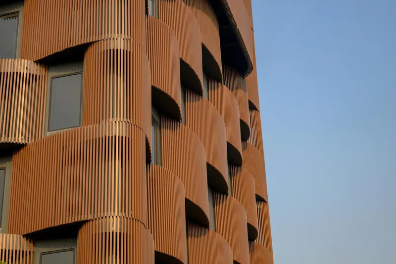 Curved facade clad in vertical terracotta fins with recessed balconies under afternoon light