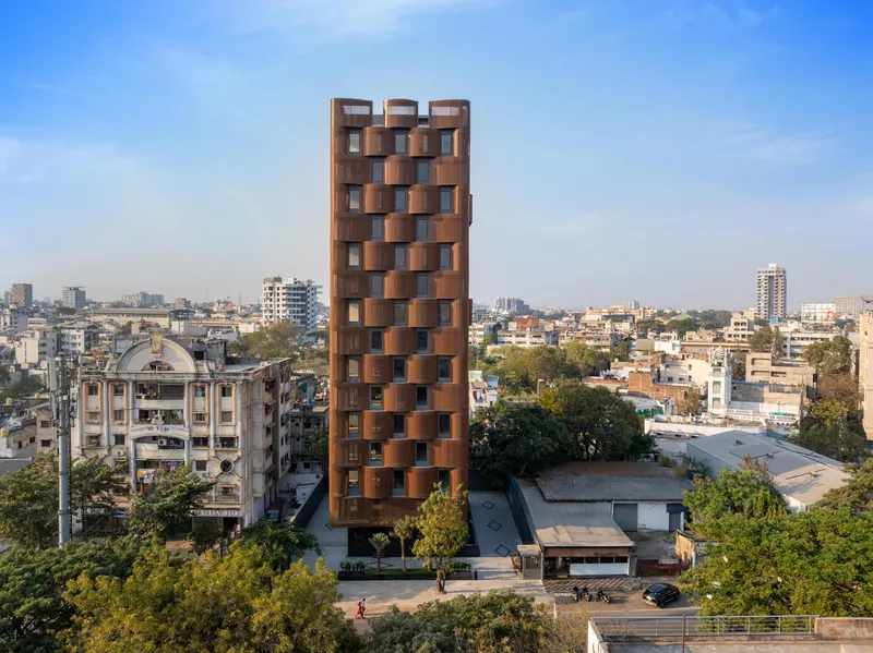 Aerial view of the ribbed terracotta facade tower rising above a dense urban neighborhood with trees