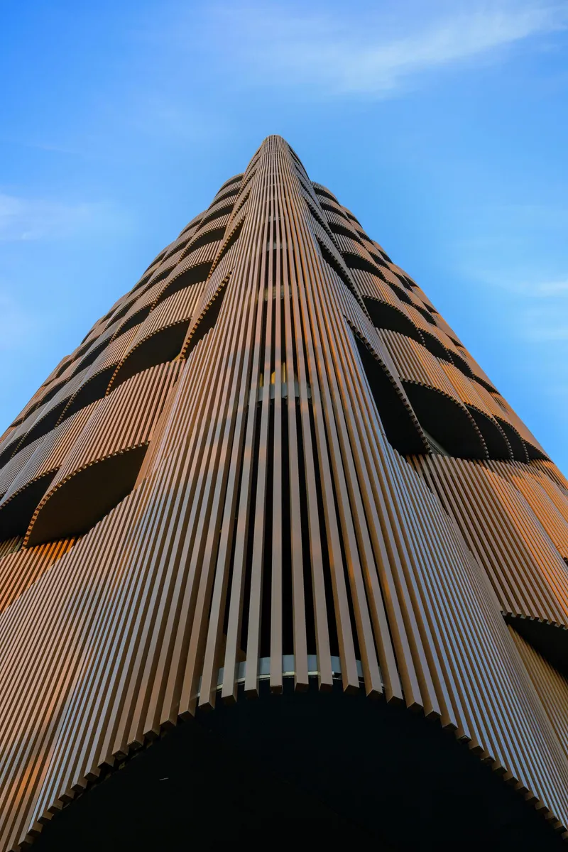 Worm's-eye view of the vertical terracotta ribs wrapping the tower corner in afternoon light