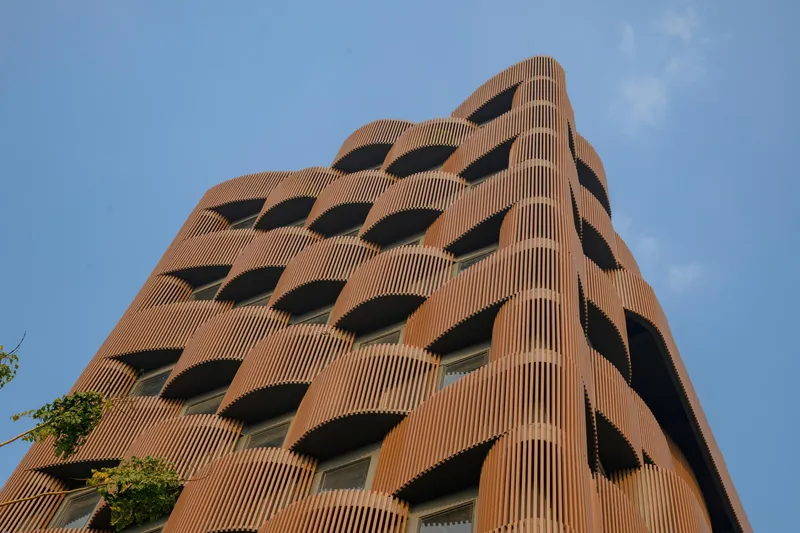 Upward view of the terracotta ribbed facade with staggered recessed balconies under clear blue sky