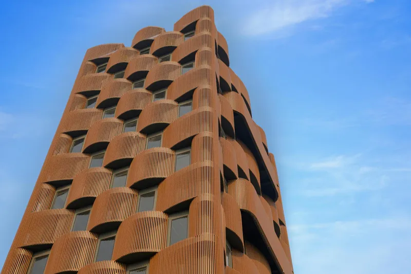 Tower facade clad in vertical terracotta fins with undulating corner geometry against wispy clouds