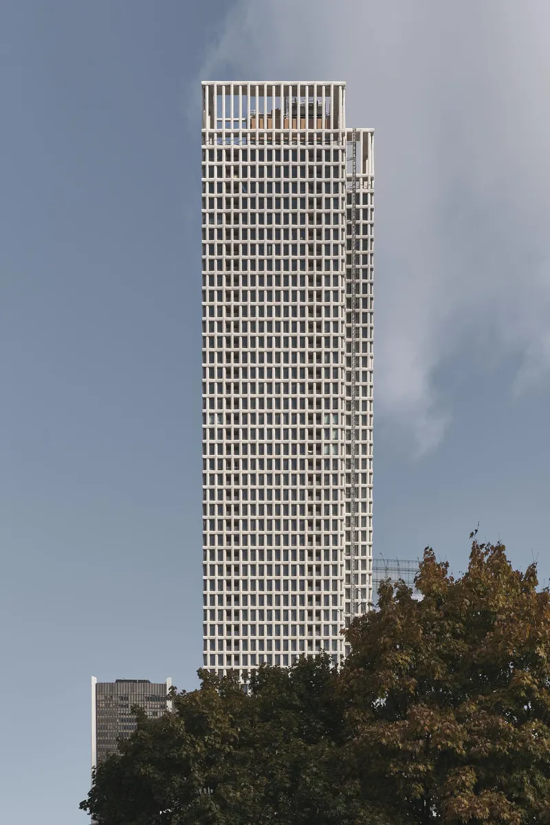 Full elevation of the slender tower rising above mature trees under an overcast sky
