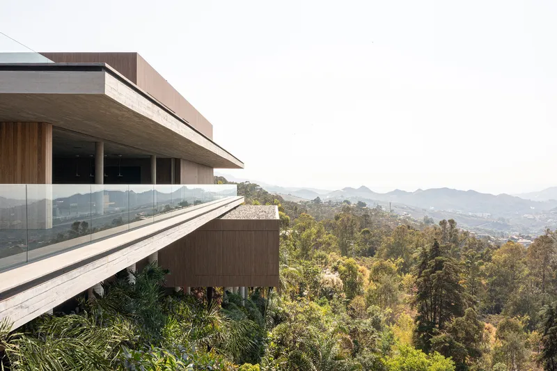 Cantilevered concrete volume with timber cladding and glass railings overlooking forested hillside and distant mountains