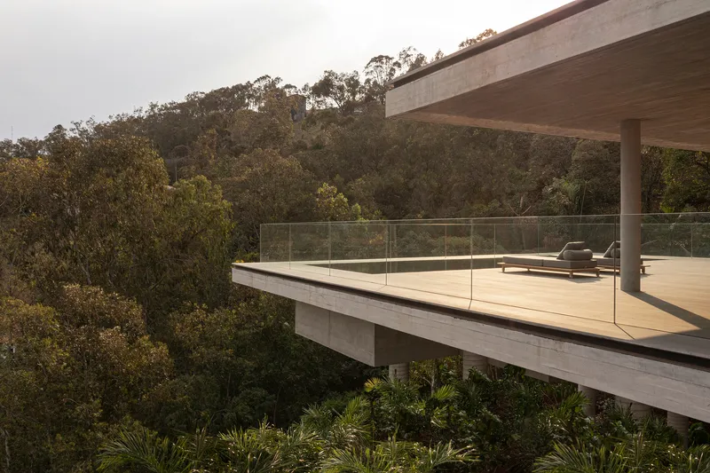 Cantilevered concrete terrace deck with glass railing suspended above dense hillside vegetation