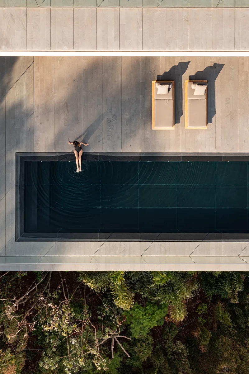 Top-down view of cantilevered pool deck with swimmer at the edge above treetops