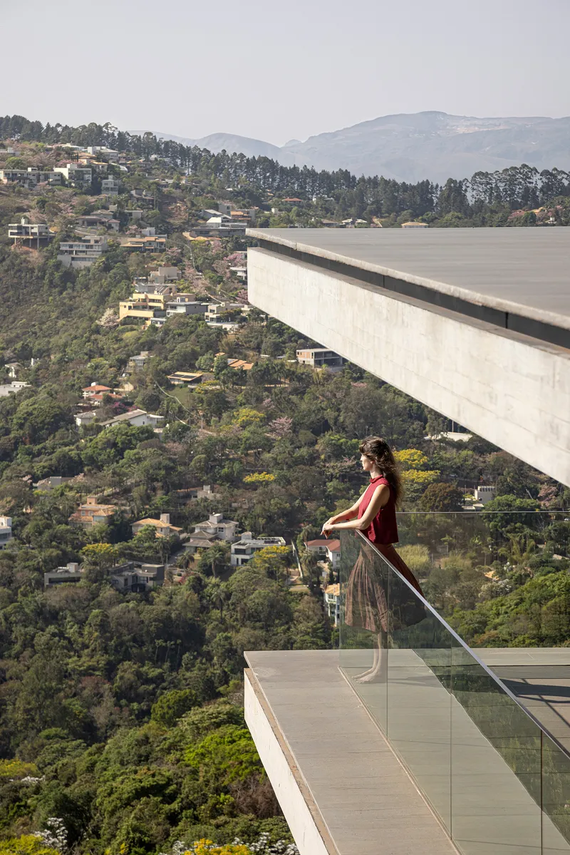Cantilevered concrete terrace with glass balustrade overlooking a forested hillside dotted with houses
