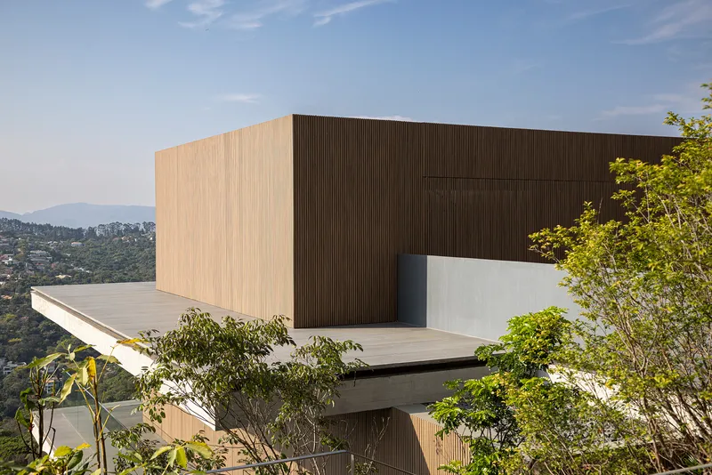 Stacked volumes clad in vertical timber slats and concrete with planted terraces and distant hills