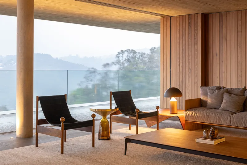 Living area with timber ceiling and cylindrical column framing a misty valley view through floor-to-ceiling glass