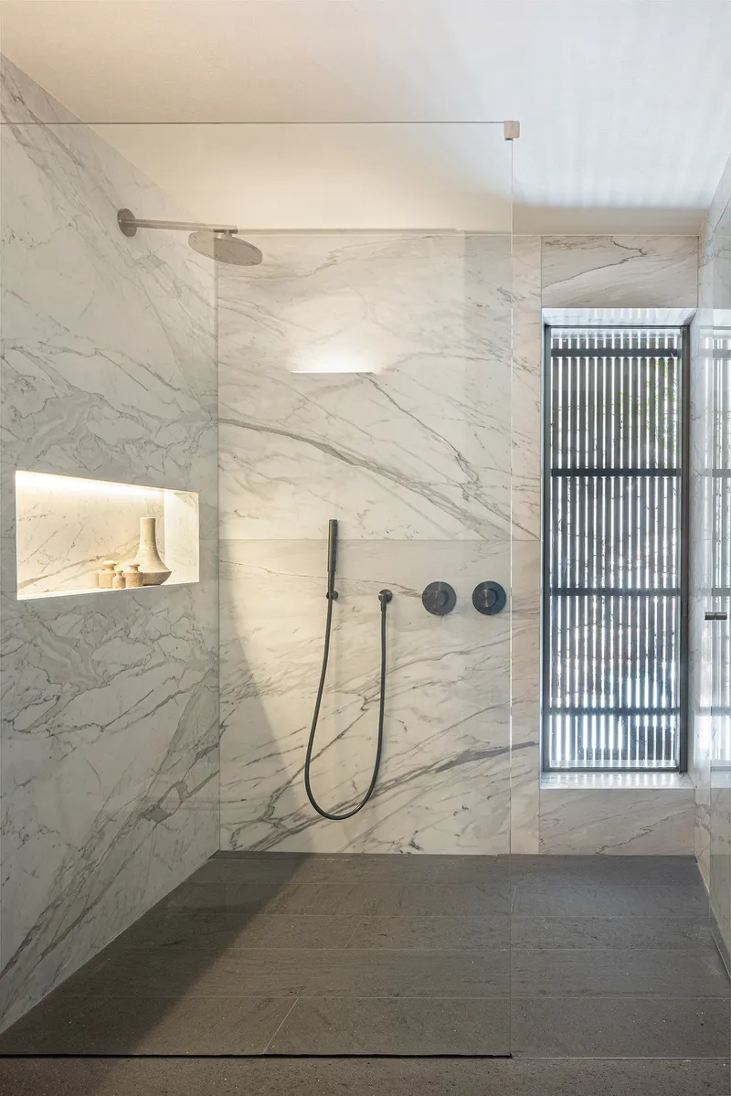 Bathroom shower enclosure clad in white marble with recessed niche and vertical louvered window