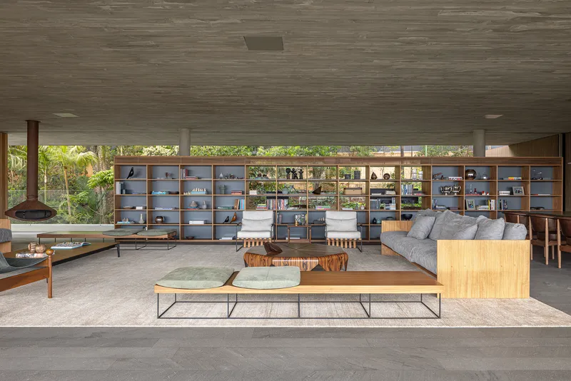 Open living space with floor-to-ceiling shelving wall and concrete ceiling overlooking lush vegetation