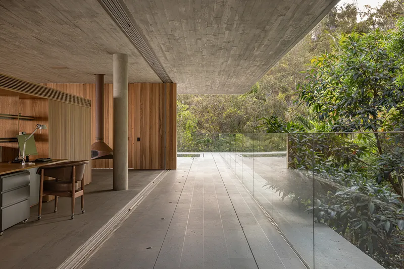 Glass-walled corridor with concrete ceiling and timber workstation opening to treetops