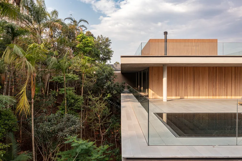Timber clad volume with cantilevered overhang and glass balustrade adjacent to lush hillside vegetation
