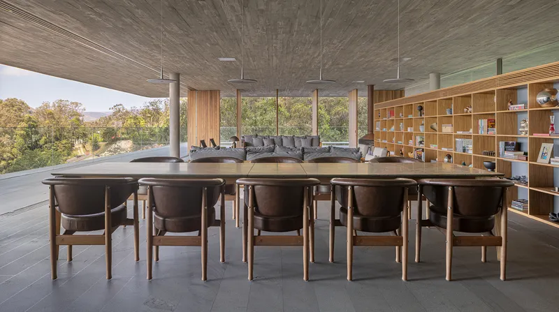 Open dining area with long table and timber chairs beneath a wood-panelled ceiling overlooking forested hills