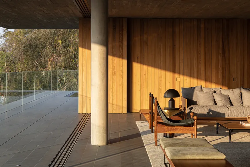 Covered terrace with cylindrical concrete column and vertical timber cladding bathed in afternoon sunlight