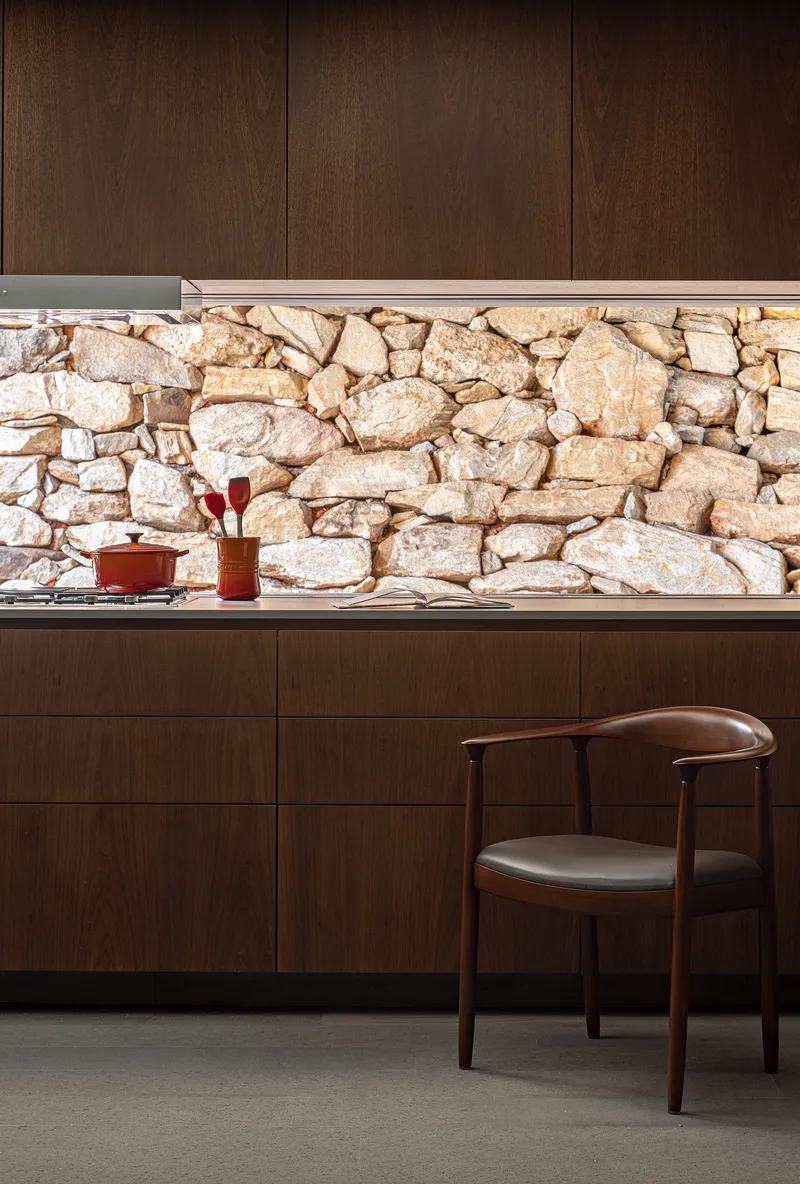 Kitchen counter with exposed stone wall backsplash beneath dark timber cabinetry and integrated task lighting