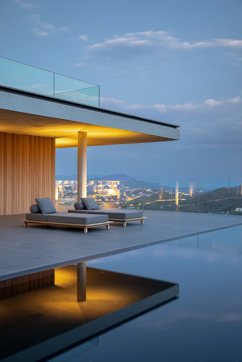 Poolside terrace with glass-edged canopy, timber cladding and lounge seating overlooking the city at dusk