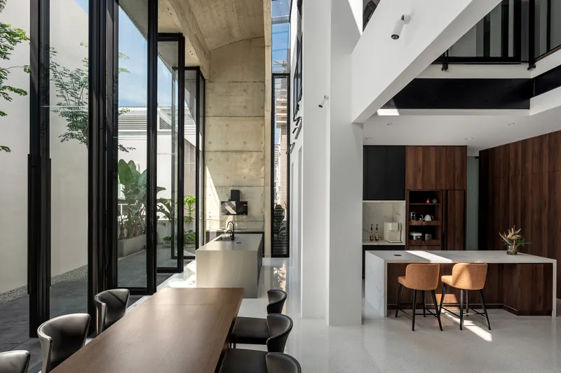 Double-height dining and kitchen space with exposed concrete beam and full-height glazing onto courtyard
