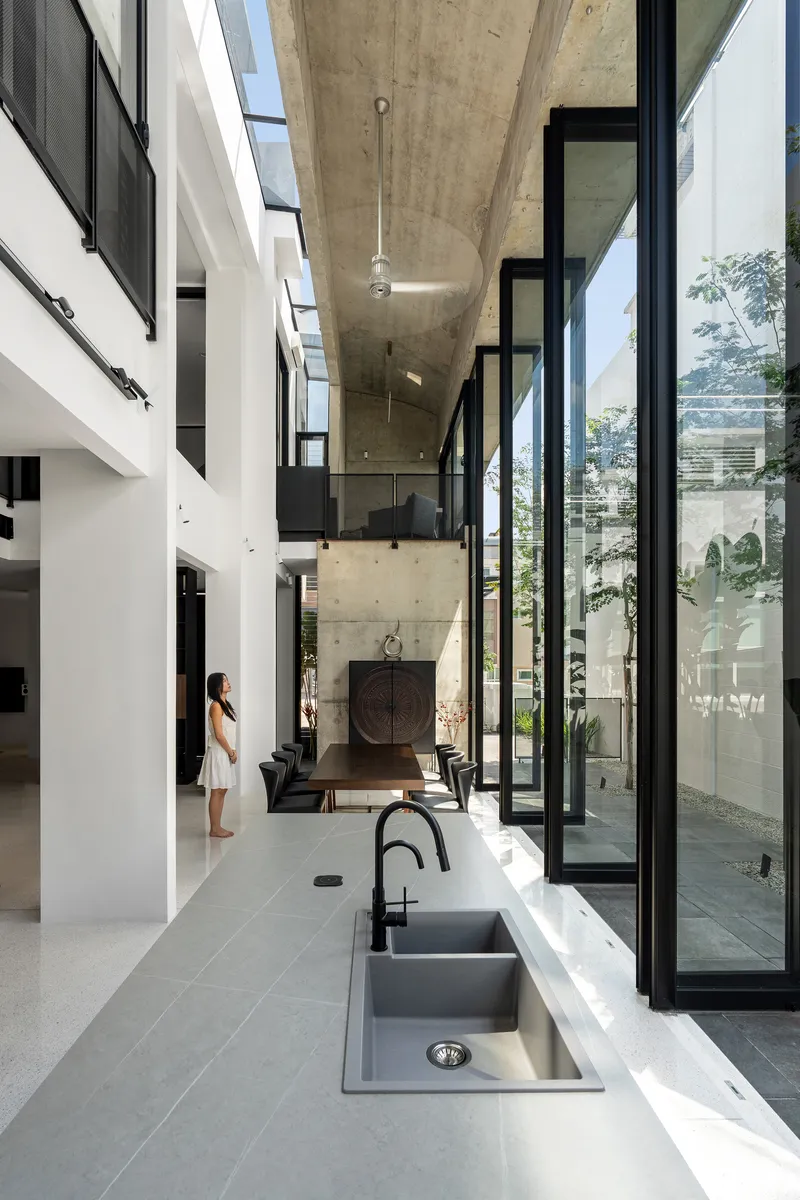White kitchen counter with integrated sink overlooking double-height courtyard with exposed concrete ceiling and clerestory windows