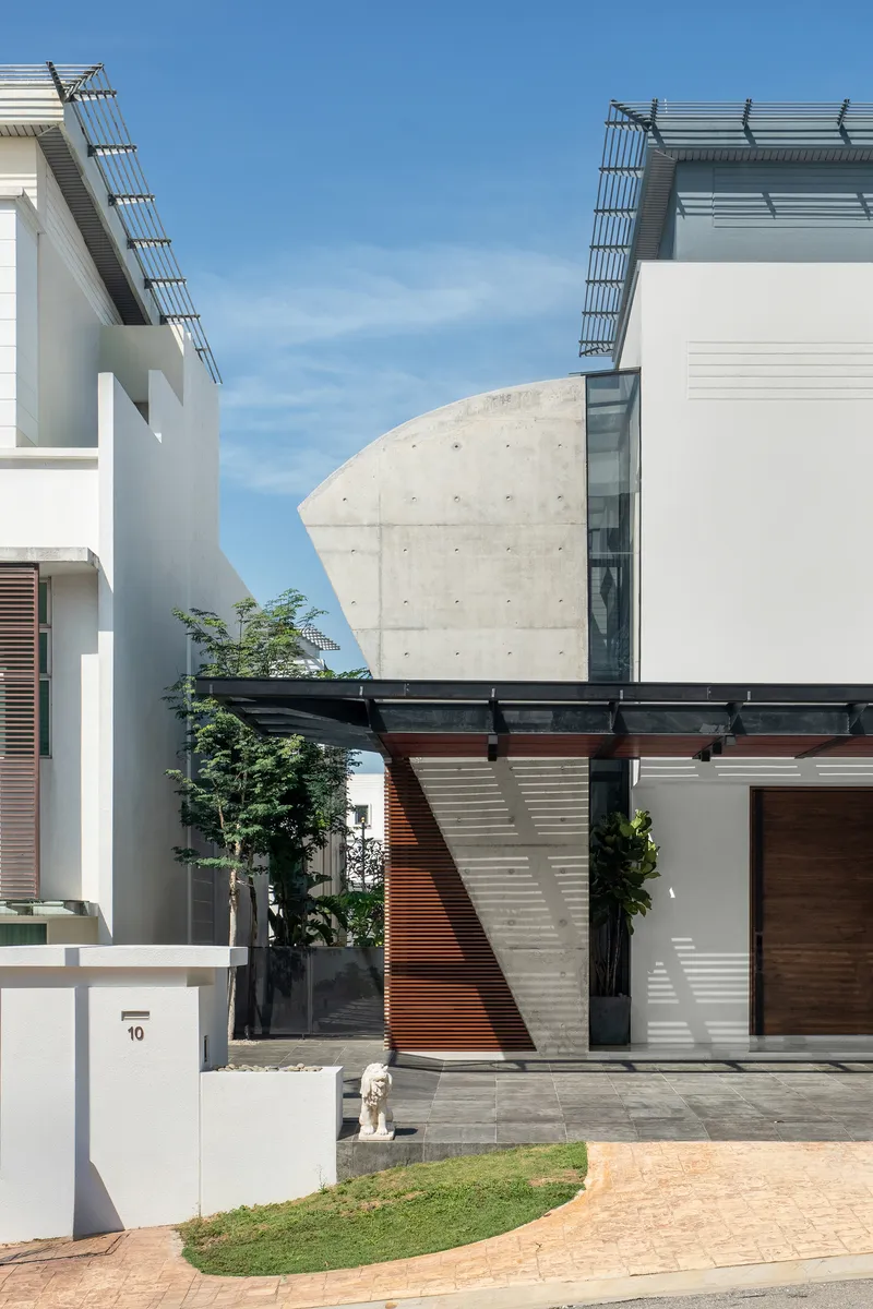 Cantilevered concrete volume with tie-hole marks above a courtyard entry framed by timber screens