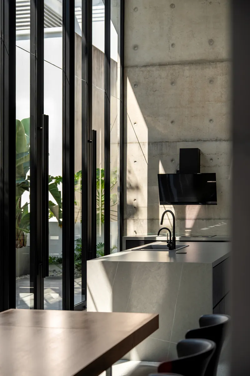 Kitchen island with integrated sink beneath vertical black steel screens opening to a planted courtyard