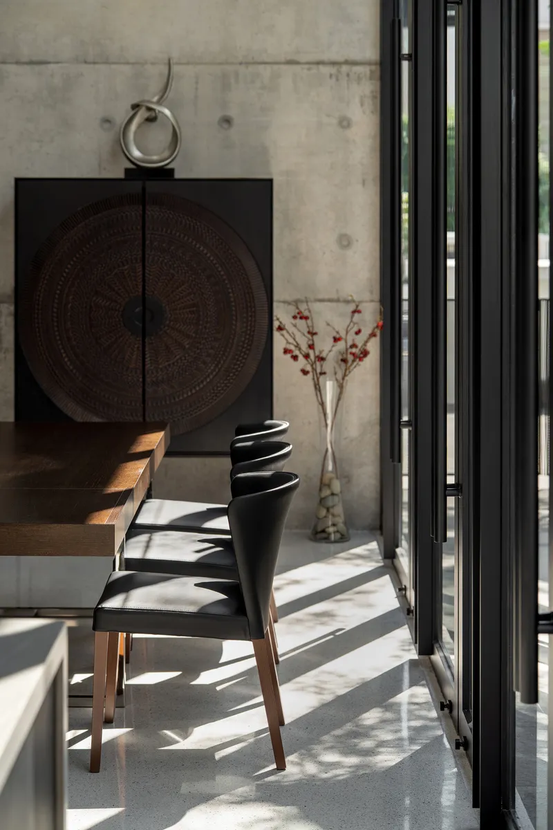 Dining chair and carved cabinet against exposed concrete wall with sunlight filtering through vertical screens
