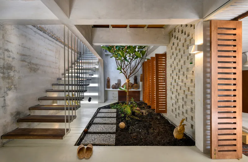 Entry foyer with cantilevered concrete staircase, central tree in planted bed, and slatted timber screens