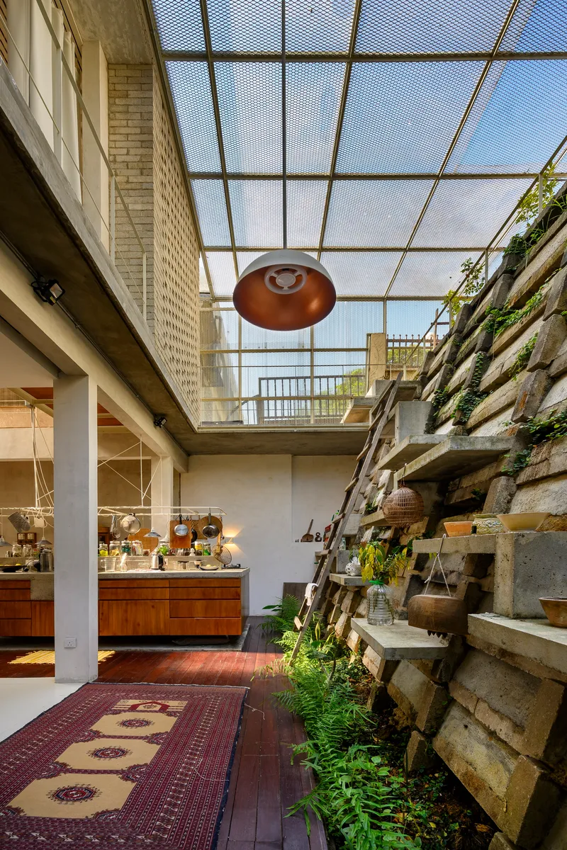 Double-height living space with mesh skylight, copper pendant, and terraced concrete block planter wall