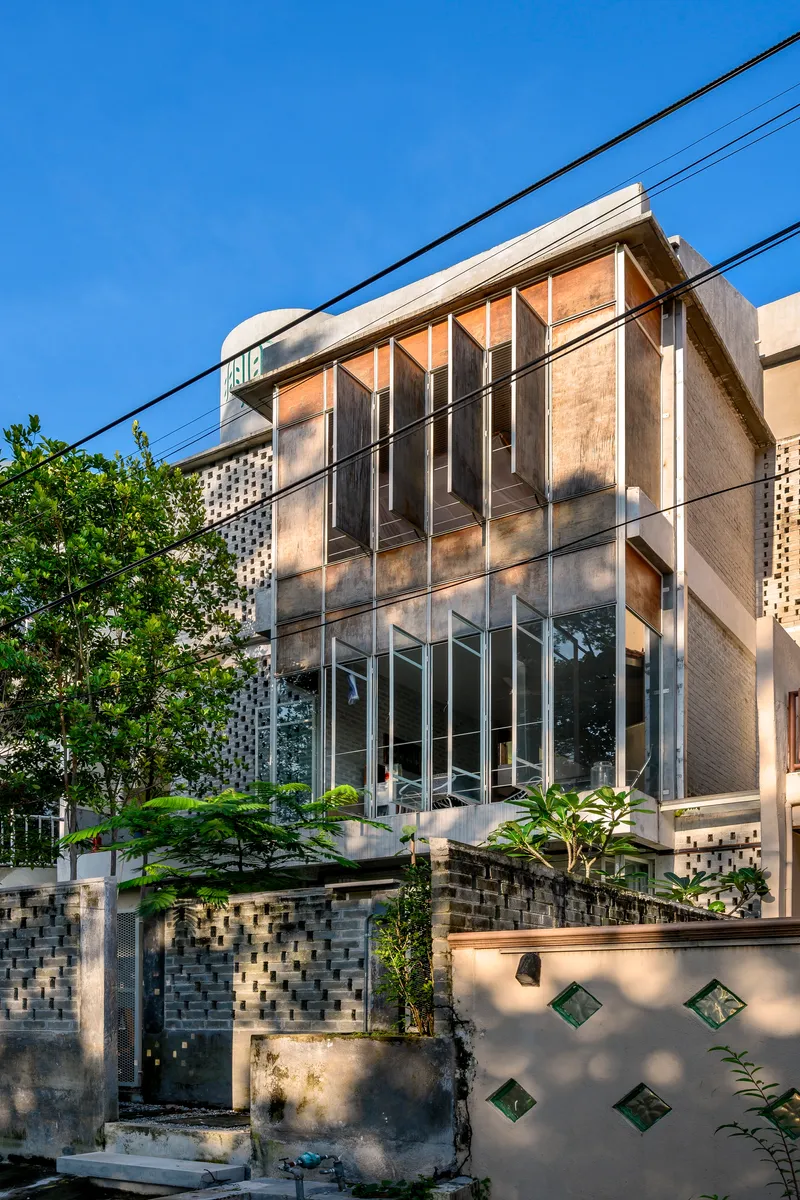Street facade with layered corrugated metal screens, perforated brick base wall, and overhead power lines