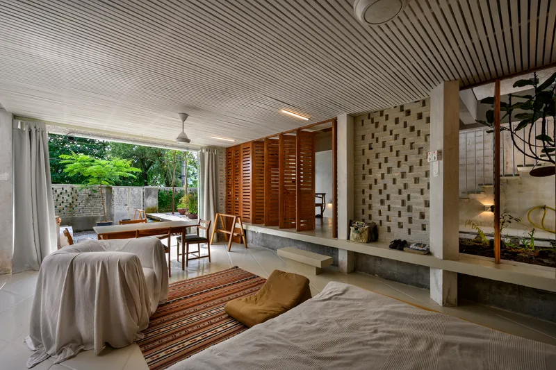 Living area with slatted ceiling opening to a planted terrace framed by white curtains