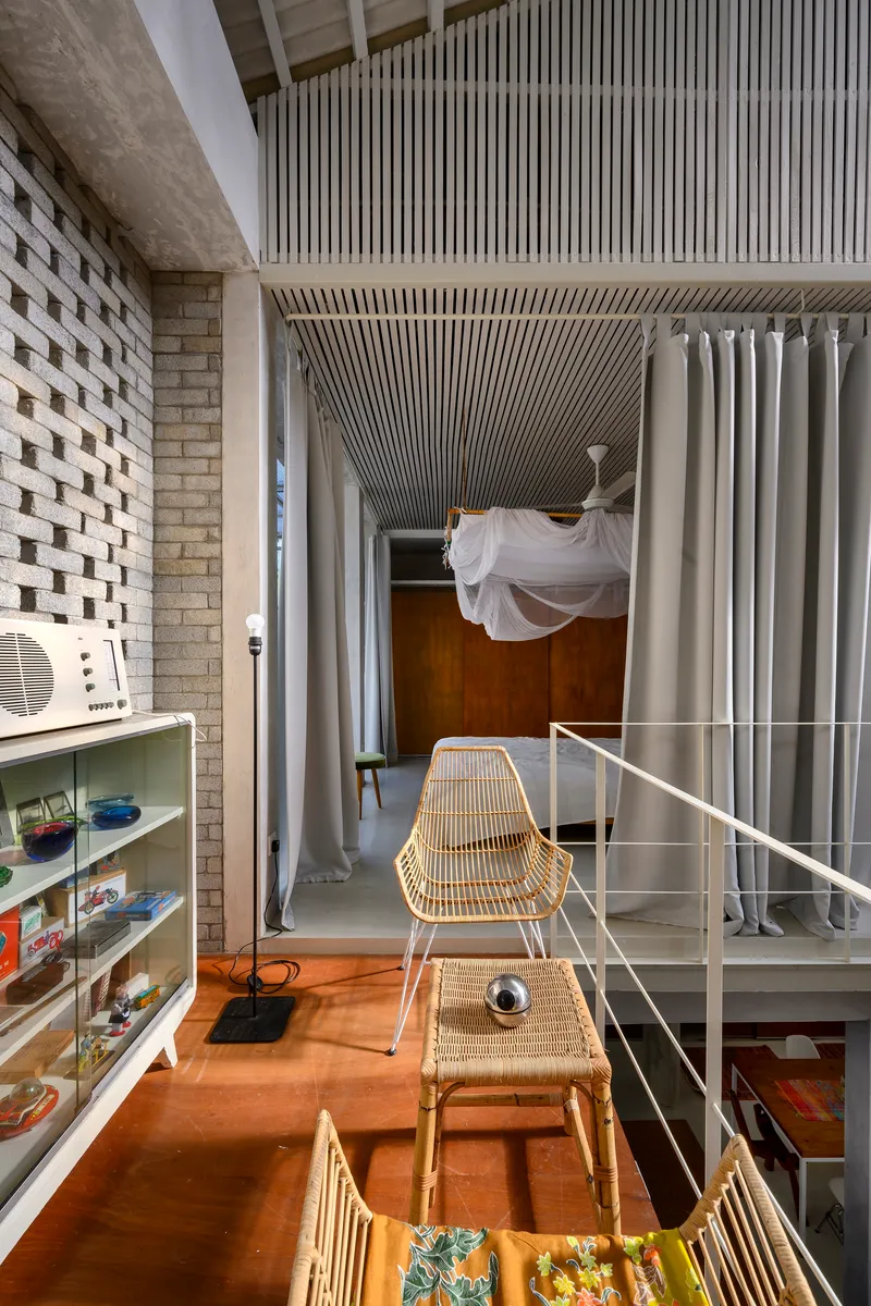 Double-height interior with woven rattan furniture and perforated brick wall alongside a suspended hammock