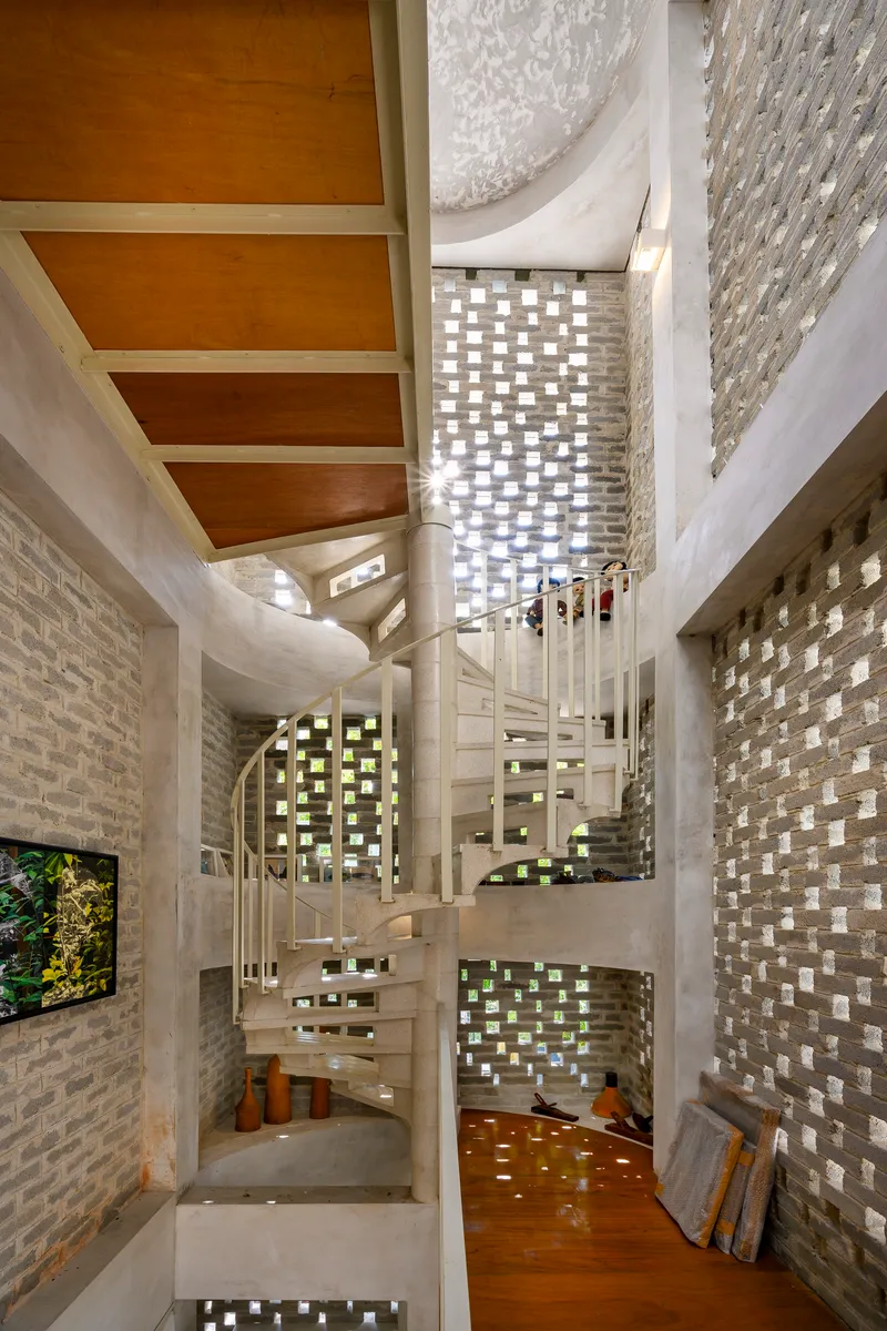 White spiral staircase surrounded by perforated brick walls filtering daylight into the interior void