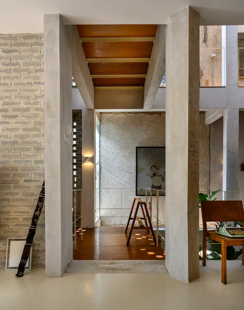 Concrete portal framing a view through interconnected rooms with timber ceiling beams and warm afternoon light