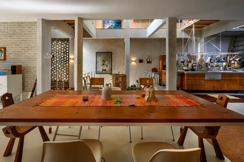 Dining table beneath exposed concrete beams and clerestory windows with perforated brick wall at left