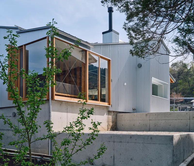 Exterior view of corrugated metal cladding and timber-framed glazing above a concrete base with young trees