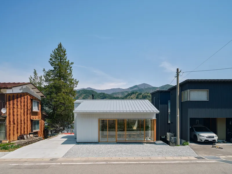 Street view of the low-slung white metal structure with glazed facade facing distant mountains