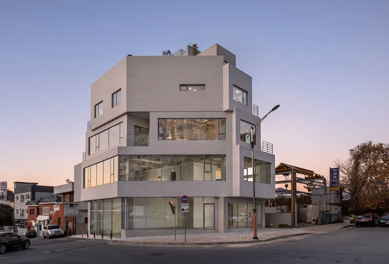 Corner view of the stacked white volumes with floor-to-ceiling glazing at dusk