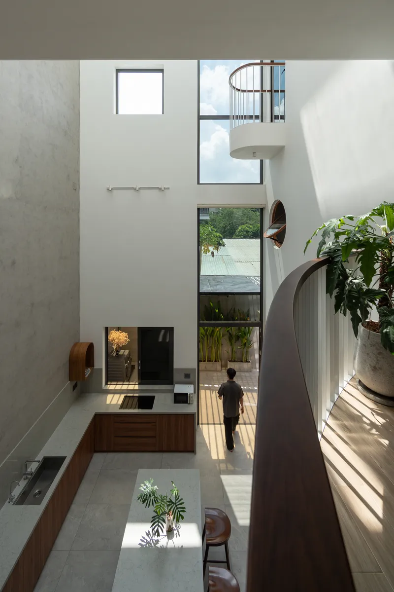 Vertical void showing stacked windows, spiral stair guard, and child walking through sunlit ground floor