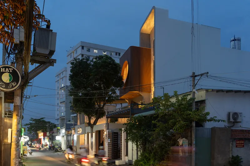 Street corner view of the timber-clad volume and circular opening at twilight beside a tree