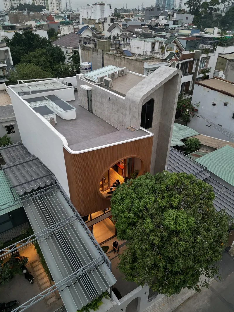 Aerial view of concrete rooftop terrace with timber-clad volume and curved opening overlooking dense neighborhood