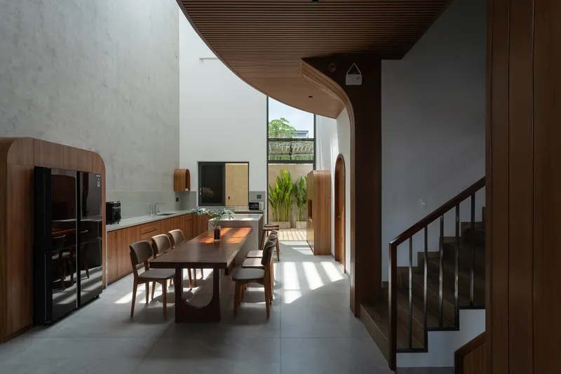 Dining area with timber-slatted curved ceiling and arched opening framing view to planted courtyard beyond